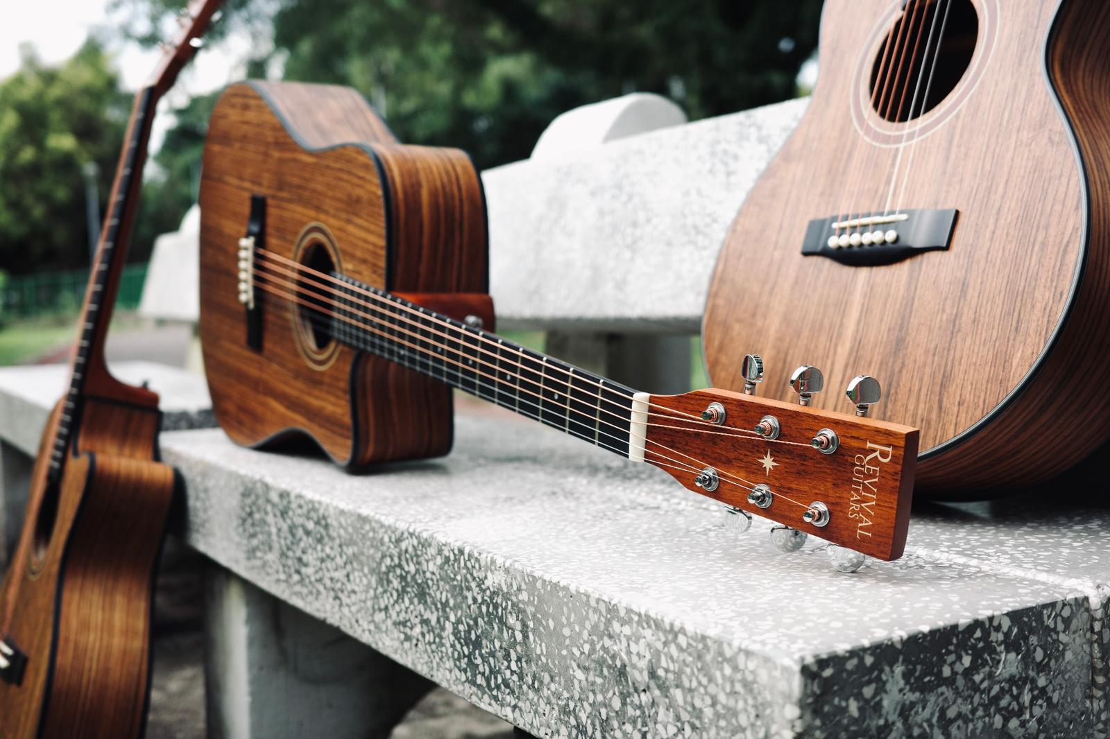 Three Revival Guitars walnut acoustic guitars resting on a park bench